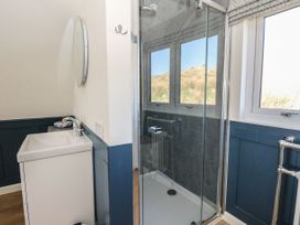 A bathroom with a sink and mirror next to a glass-enclosed shower and window with views of a grassy hill at Scarba in Cullipool Isle Of Luing