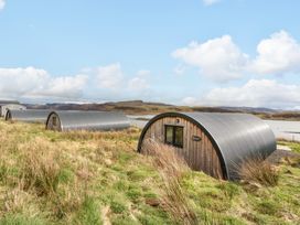Curved metal and wood cabins on grassy land near water with hills in the background at Torsa Cullipool Isle Of Luing