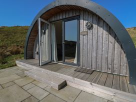 A curved wooden cabin with open glass doors and stone patio outdoors at Torsa Cullipool Isle Of Luing