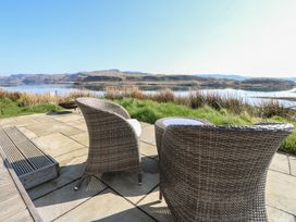 An outdoor patio with wicker chairs and a small table overlooking water and hills at Torsa Cullipool Isle Of Luing
