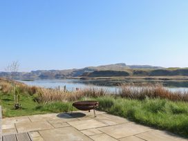 A patio with a fire pit overlooking a body of water and hills at Torsa in Cullipool Isle Of Luing