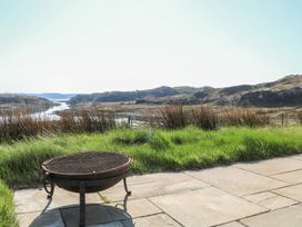 A fire pit on a stone patio with grassy area and hills in the background at Torsa Cullipool Isle Of Luing