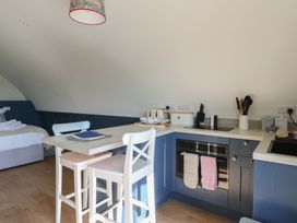 A kitchen area with blue cabinets white chairs a countertop oven and a bed in the background at Torsa Cullipool Isle Of Luing