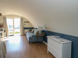 A room with a blue sofa a white chest of drawers a side table and a door with curtains leading outside at Torsa in Cullipool Isle Of Luing