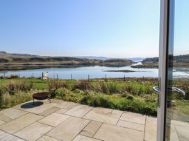 A view of a tiled patio with a fire pit and grassy area overlooking a body of water and hills at Torsa Cullipool Isle Of Luing