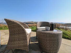 Two wicker chairs and a wicker table with a coffee pot and cup on a stone patio overlooking a grassy landscape at Torsa Cullipool Isle Of Luing