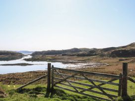 A wooden gate opens to a grassy area with a body of water and hills in the background at Torsa Cullipool Isle Of Luing