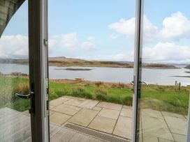 A view of a grassy landscape and a body of water through open glass doors at Fladda in Cullipool Isle Of Luing