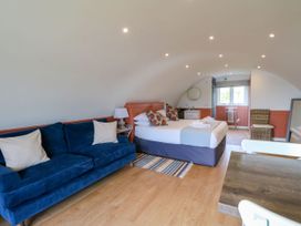 A bedroom with a blue sofa bed a bed with pillows a wooden table and chair a mirror and window at Fladda in Cullipool Isle Of Luing