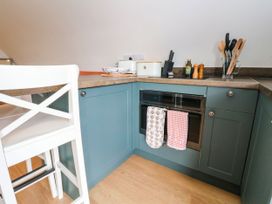 A kitchen corner with blue cabinets a built-in oven towels hanging a white chair and kitchen utensils on the counter at Fladda Cullipool Isle Of Luing