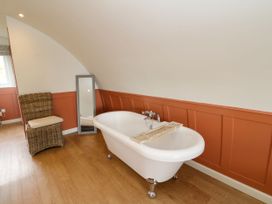 A bathroom with a freestanding bathtub a wicker chair and a standing mirror at Fladda in Cullipool Isle Of Luing