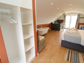 A bedroom with a bed towels a wardrobe bathtub kitchen area and glass doors at Fladda in Cullipool Isle Of Luing