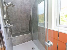 A shower area with a built-in seat handheld showerhead and a glass door in a bathroom at Fladda in Cullipool Isle Of Luing