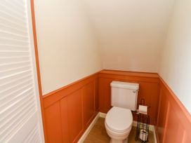 A small bathroom with a white toilet and a black toilet paper holder against orange panel walls at Fladda in Cullipool Isle Of Luing