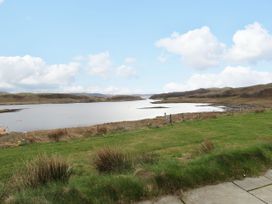 A grassy field with a wooden fence overlooking a body of water and hills under a partly cloudy sky at Fladda in Cullipool Isle Of Luing