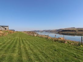 A grassy lawn beside a fenced waterfront with hills in the background and a wooden building on the left at Fladda in Cullipool Isle Of Luing