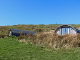 Two curved metal and wooden structures on grassy land with hills and clear blue sky at Losal Cullipool Isle Of Luing