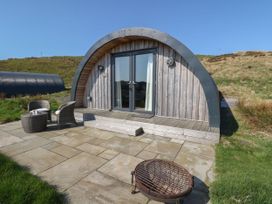 A wooden curved cabin with glass doors a patio with chairs and a fire pit at Losal Cullipool Isle Of Luing