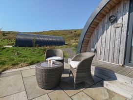 An outdoor seating area with two wicker chairs and a table with two mugs in front of a wooden pod at Losal in Cullipool Isle Of Luing