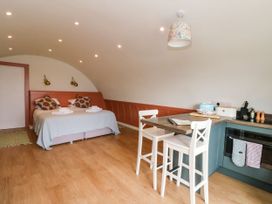 A room with a double bed with patterned cushions and folded towels a kitchen counter with two chairs and kitchen appliances at Losal in Cullipool Isle Of Luing