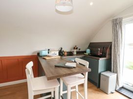 A kitchen with a wooden table and two white chairs by a glass door with patterned curtains at Losal Cullipool Isle Of Luing
