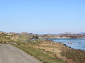 A coastal road with grassy hills boats on the water and buildings at Losal Cullipool Isle Of Luing
