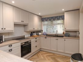 A kitchen with beige cabinets a built in oven a sink under a window and wooden herringbone floor at 6 Uppergate Street Rose Cottage in Conwy