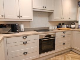 A kitchen with white cabinets a built in oven an electric stove a microwave kettle toaster and cutting board at 6 Uppergate Street Rose Cottage in Conwy