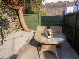 An outdoor seating area with a round wicker table two wicker chairs a champagne bottle and flutes near a stone wall and green wooden fence at 6 Uppergate Street Rose Cottage Conwy