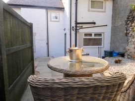 A small outdoor patio with a round glass table and wicker chairs next to a white house at 6 Uppergate Street Rose Cottage in Conwy