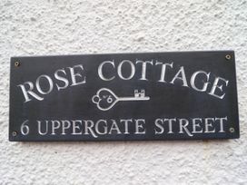A black address plaque with white engraved text reading Rose Cottage 6 Uppergate Street on a textured white wall at 6 Uppergate Street Rose Cottage Conwy