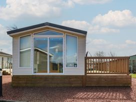 A small mobile home with large windows and a wooden deck on a gravel surface at Plot 6 near Armathwaite