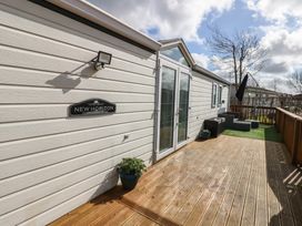 An outdoor wooden deck area with potted plants patio furniture and a white exterior wall with glass doors at Plot 6 near Armathwaite