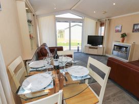 A dining table set with plates glasses and a wine bottle in a living room with sofas a television and a fireplace at Plot 6 near Armathwaite