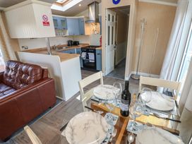 A kitchen and dining area with a glass table set for four with plates and wine near a brown leather sofa and blue kitchen cabinets at Plot 6 near Armathwaite