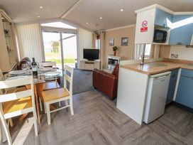 A kitchen and dining area with a glass table with chairs a small fridge and microwave a living area with sofas a tv and a fireplace at Plot 6 near Armathwaite