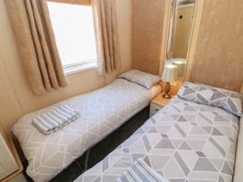 A small bedroom with two single beds towels on each bed a bedside table with lamp and a mirror on the wall at Plot 6 near Armathwaite