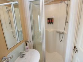 A bathroom with a shower, sink, mirror, and toiletries at Plot 6 near Armathwaite