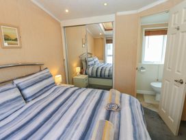 A bedroom with a striped bedspread and towels on the bed a bedside table with a lamp and a mirrored closet door and an open door showing a bathroom at Plot 6 near Armathwaite