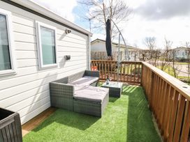 A wooden deck outside a mobile home with a wicker sofa and table on artificial grass near Armathwaite