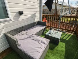 A patio with a gray outdoor sofa a glass top coffee table with wine glasses on artificial grass at Plot 6 near Armathwaite