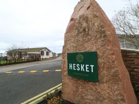 A large stone with a Hesket Caravan Park sign next to a road with houses and speed bumps near Armathwaite