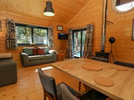 A wooden interior living room with a dining table chairs sofas a wood stove and large windows at Esk Lodge Salen Isle Of Mull