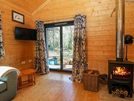 A wooden room with a wood burning stove burning fire a wall mounted television and glass doors with curtains at Esk Lodge in Salen Isle Of Mull