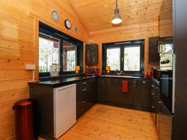 A kitchen with black cabinets a small white fridge two windows above the countertops and wooden walls and ceiling at Esk Lodge in Salen Isle Of Mull