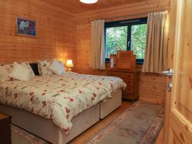 A bedroom with a bed floral bedding a wooden dresser with a mirror and a window at Esk Lodge Salen Isle Of Mull