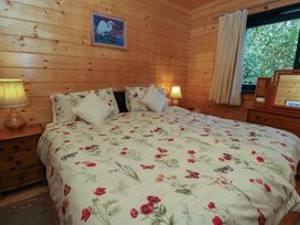 A bedroom with a double bed floral bedding bedside tables with lamps wooden walls and a window at Esk Lodge Salen Isle Of Mull
