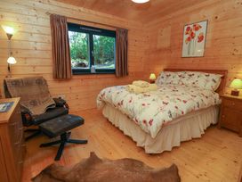A bedroom with a bed with floral bedding two bedside tables lamps an armchair with footrest a chest of drawers window with curtains and wooden walls at Esk Lodge Salen Isle Of Mull