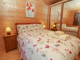 A bedroom with a bed floral bedding two bedside tables with lamps wooden walls and a large mirrored wardrobe at Esk Lodge in Salen Isle Of Mull