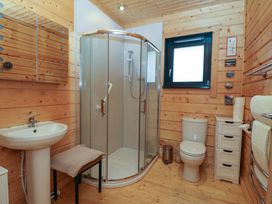 A bathroom with wooden walls and floor a glass shower enclosure a white sink a toilet a small cabinet and a window at Esk Lodge in Salen Isle Of Mull